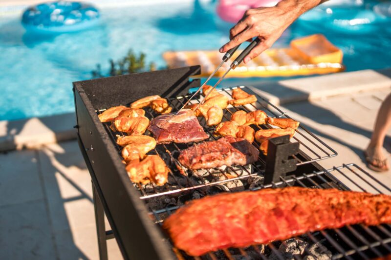 Close up on sizzling meat on the grill at a pool party