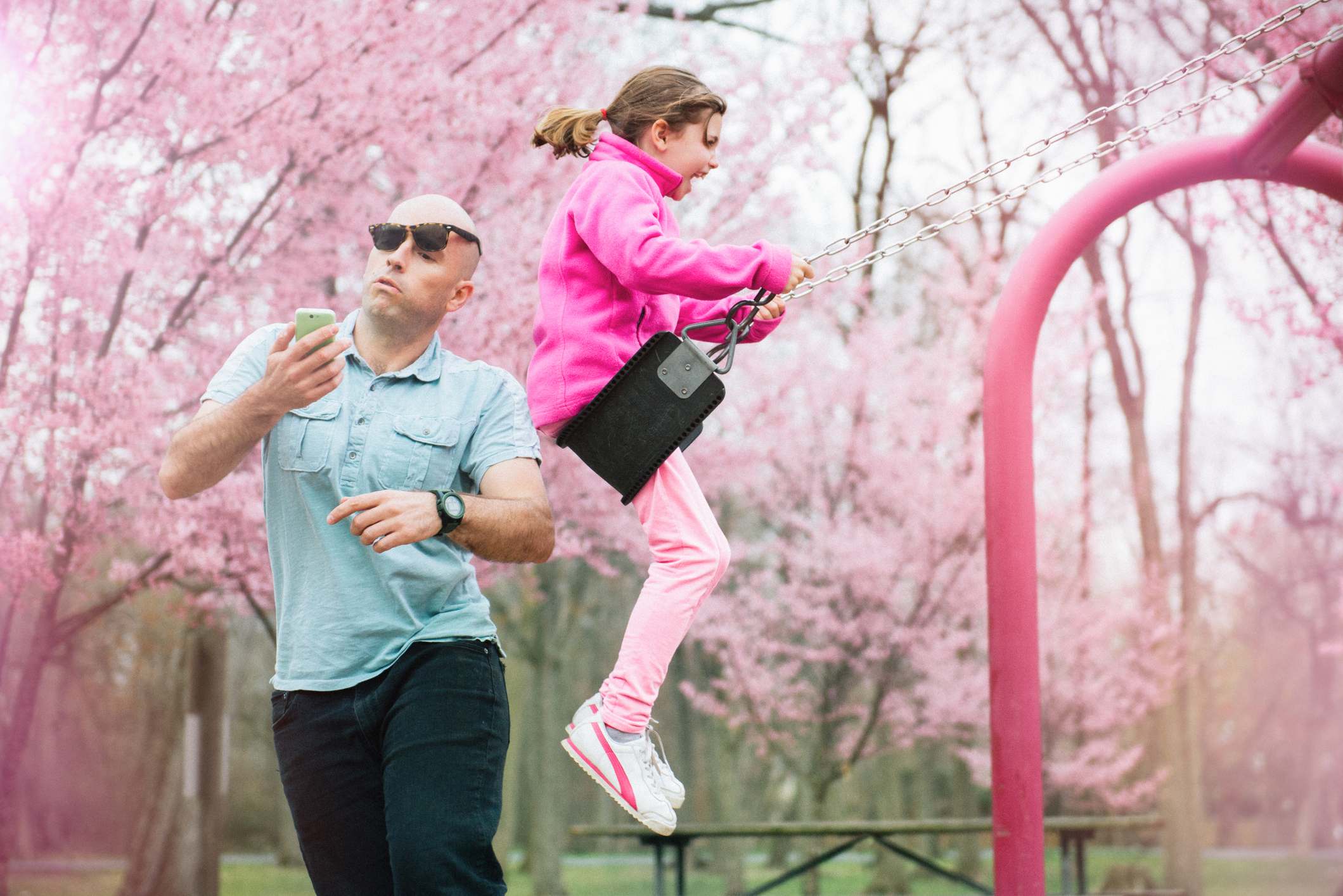 Parent gets hit by his daughter on the swing while watching smart phone.