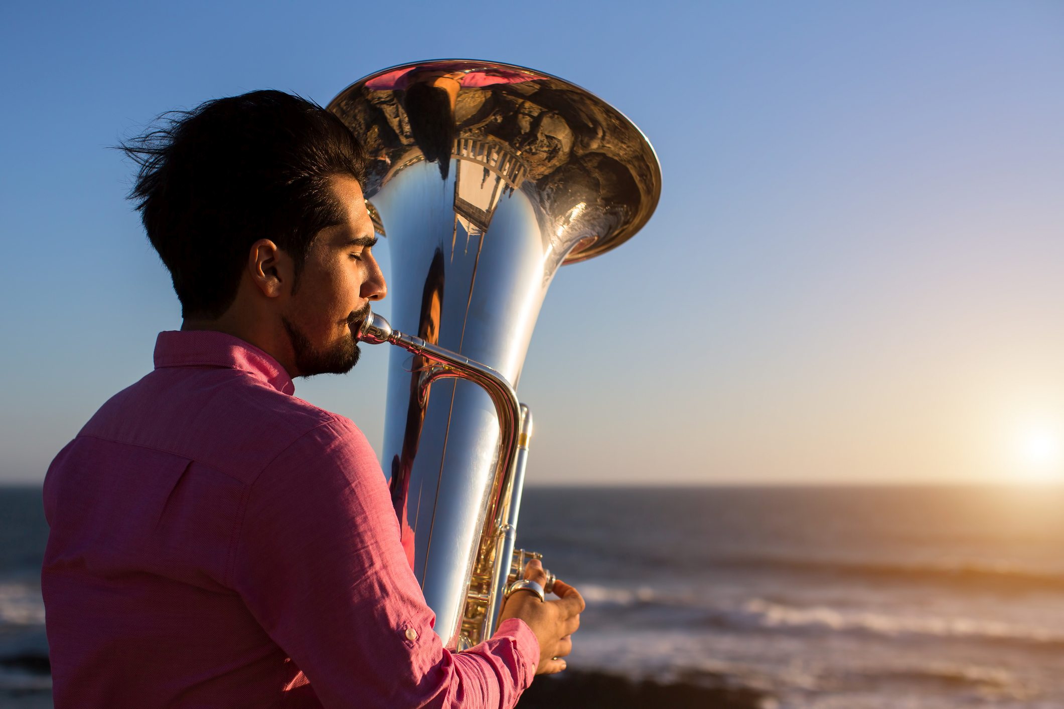 Man playing tuba on the beach looking out to sea