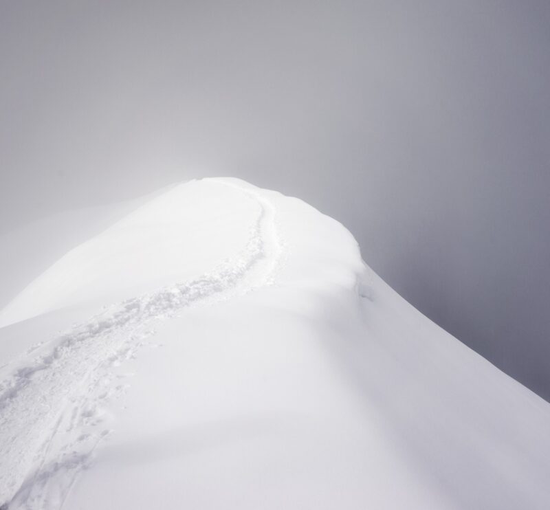 A narrow footpath on an alpine mountain ridge surrounded by thick cloud.