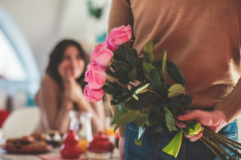Close up shot of unrecognizable male holding a bouquet of roses behind his back, about to surprise his girlfriend.
