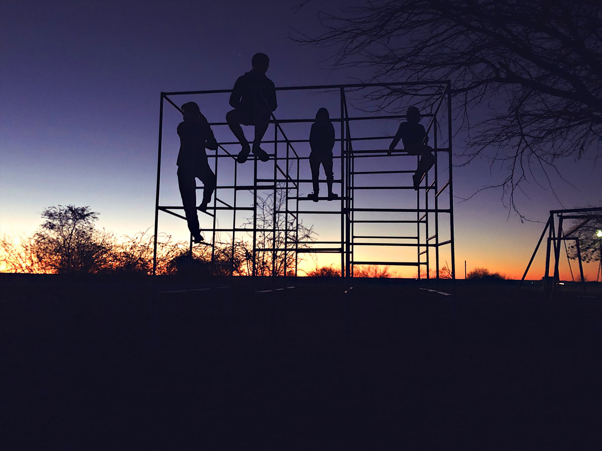 Silhouette of 4 teenage and young children on a playground jungle gym tower at dawn in Namibia Africa