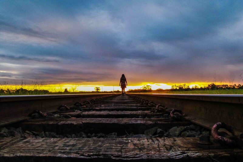 Rear View Of Woman Walking On Railroad Track Against Sky