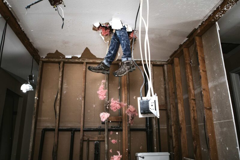 A man's feet sticking through a hole in the ceiling beside trailing cords