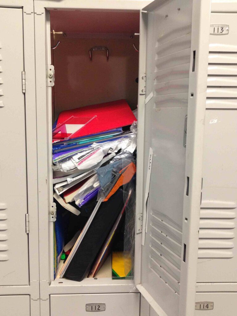 Open school locker showing a messy stack of books and papers inside