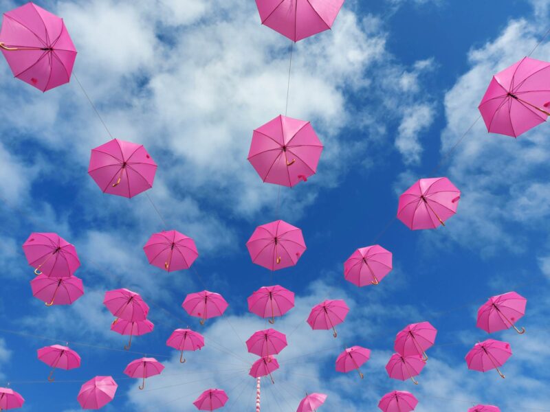 Open pink umbrellas suspended against a blue sky with white clouds