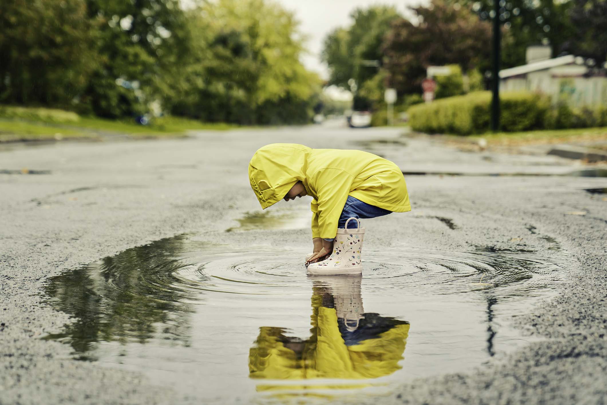 A Funny cute baby girl wearing yellow waterproof coat and boots playing in the rain