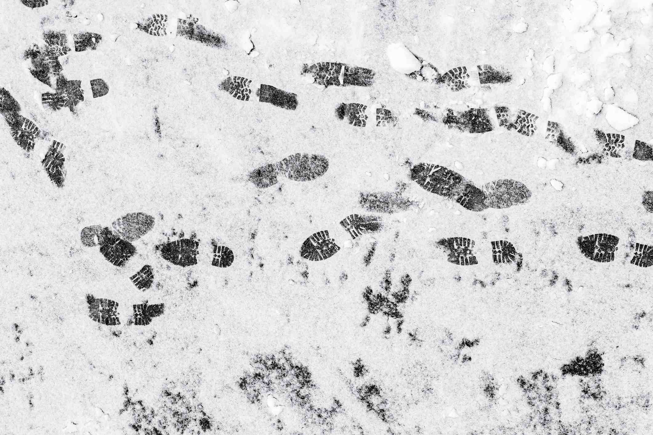 Black footprints over the snow on a gray asphalt road