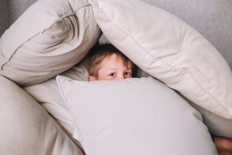 Little boy playing and hiding under pillows