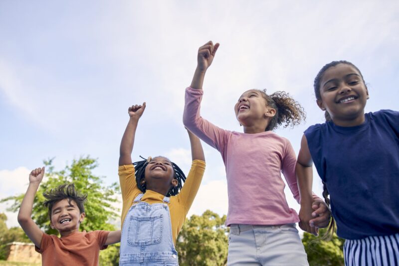 Children, energy and diversity with friends cheering together outdoor while having fun during the day. Kids, freedom or celebration with a girl and boy group playing or bonding outside in summer