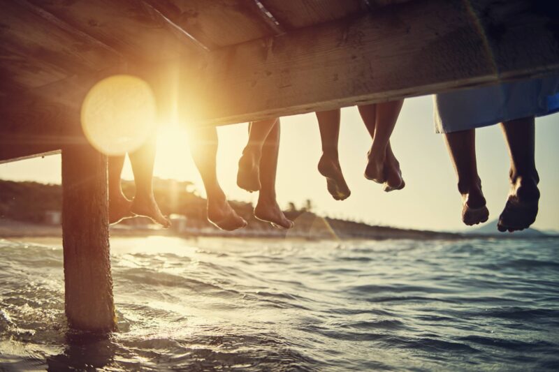 Five people having fun sitting on pier. Feet shot from below the pier. Sunny summer day evening.