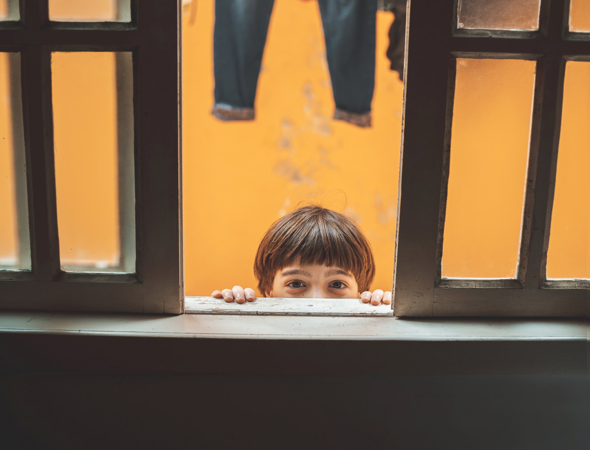 Child peeking out the window, looking at the camera.