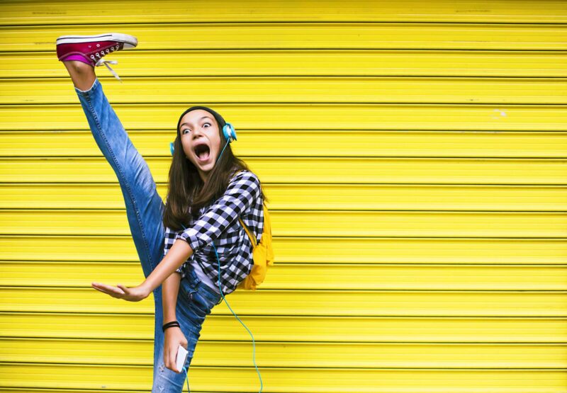 Dancing girl kicking high while standing against a yellow background