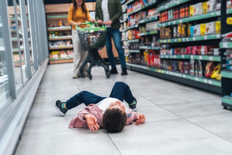 Shot of small boy lying on floor and fusses while his mom and dad shops for groceries. A capricious child lies on the ground in cry refusing to go. A little boy is lying on the ground in front of his parents and crying.