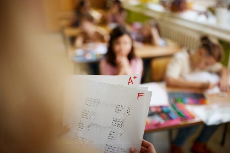 Close up of unrecognizable elementary teacher holding positive and negative test results in the classroom.